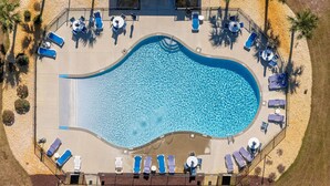 An aerial view of a swimming pool with lounge chairs and tables arranged around it, surrounded by palm trees and a sandy area. - Sunsets on the Sound + Walk to the Beach (Atlantic Beach)