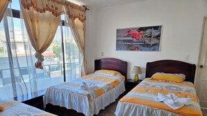 Habitació d'hotel amb dos llits, una finestra amb cortines, una tauleta de nit amb una làmpada i un quadre d'un flamenc.