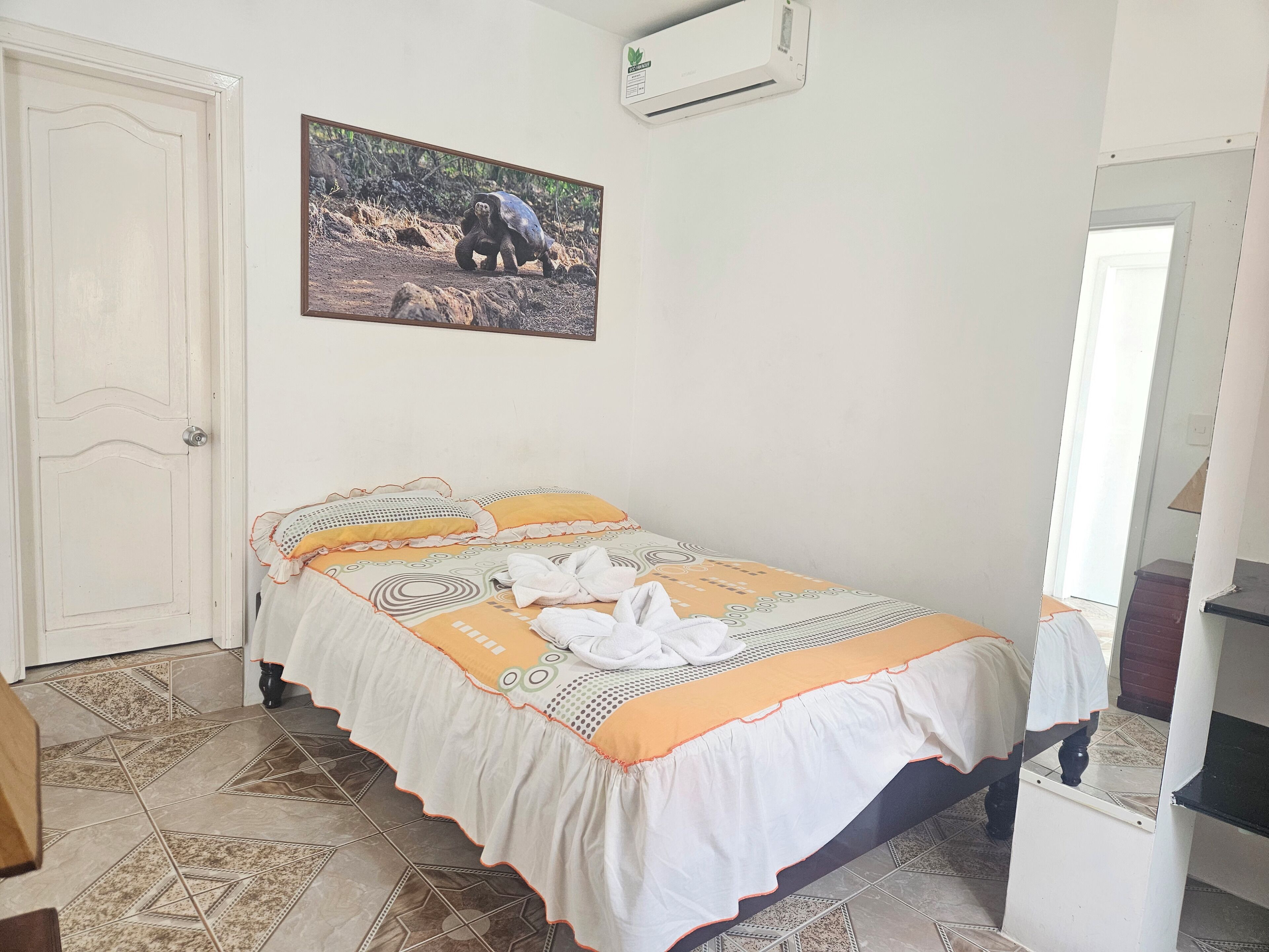 Une chambre à coucher comprenant un lit, une porte, un climatiseur fixé au mur et un tableau représentant une tortue.