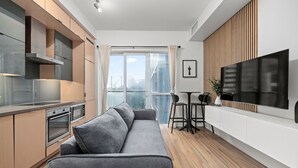 A modern kitchen with built-in appliances, a grey sofa, a dining area with a TV, and a large window with a view. - Lovely 1 BR Suite + Gym + Pool, MTCC, CN Tower (Toronto)