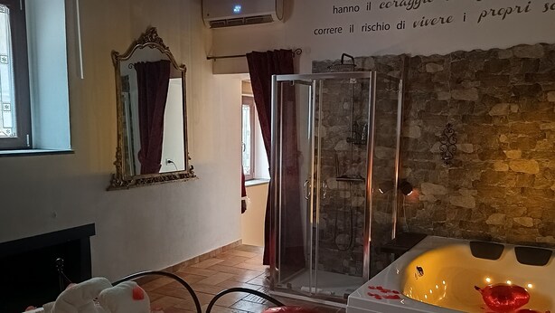 A bedroom with a bed, a glass shower enclosure, a stone wall, and a sign with Italian text. - Location Le 10&10 idromassaggio in camera Nepi VT (Nepi)