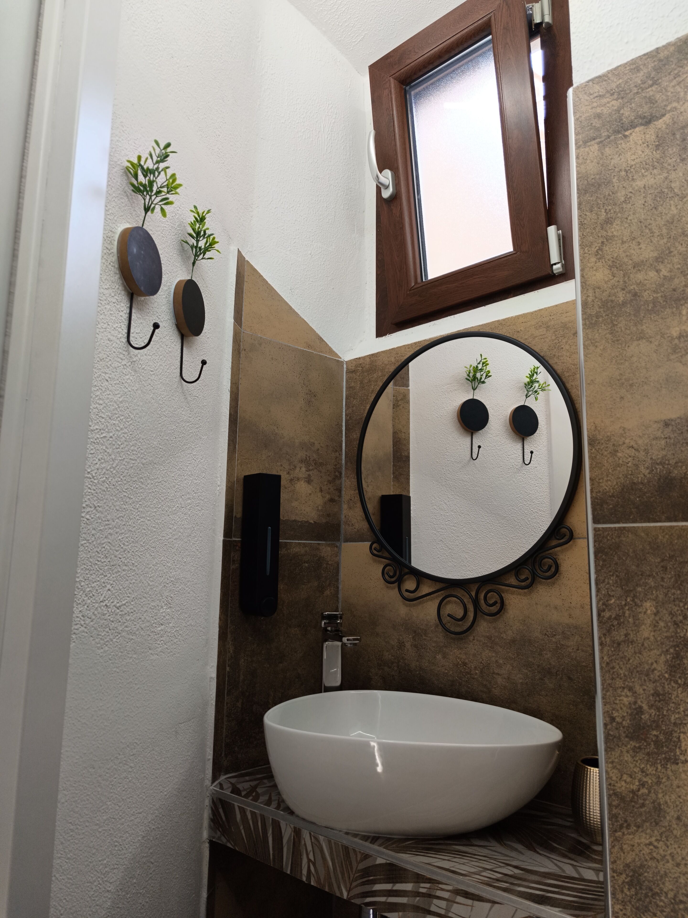 Un baño con un lavamanos blanco, un espejo redondo y una pequeña ventana sobre el espejo.
