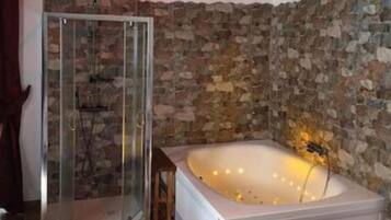 A bathroom with a stone wall, a glass shower enclosure, and a white bathtub with a golden light fixture.