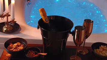 Un bain à remous avec une bouteille de champagne, deux coupes à champagne et des bols remplis de collations disposés sur un plateau.