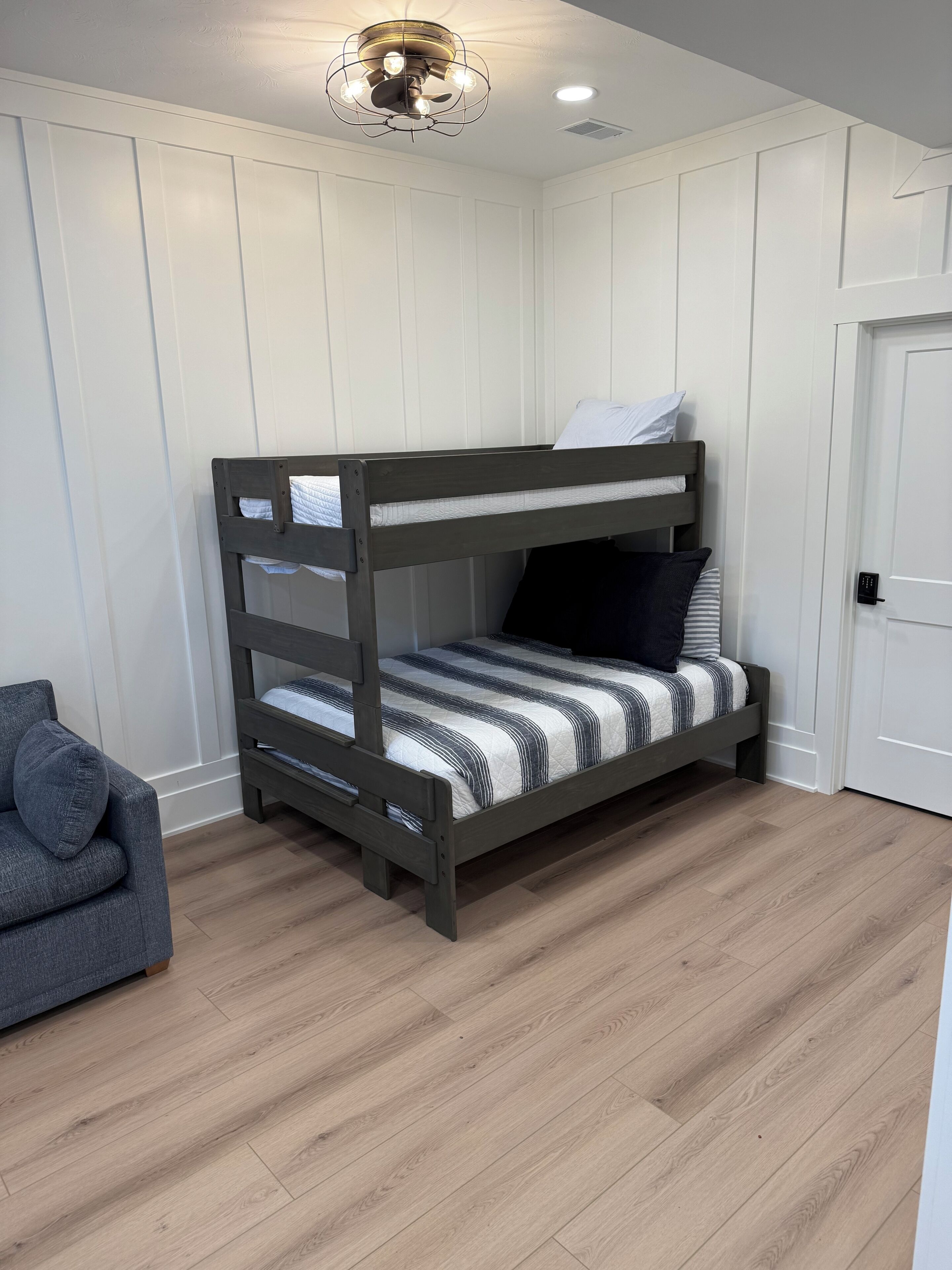 A bunk bed with a striped bedspread, a grey upholstered chair, and a white door.