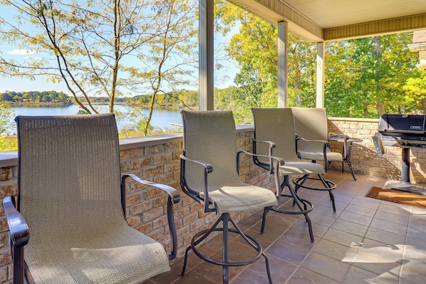 A covered patio with wicker chairs and a grill, overlooking a lake. - Goose Lake Home: 13 Mi to Michigan Int'l Speedway (Jerome)