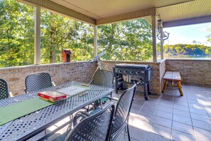 Eine Terrassensitzgelegenheit mit Tisch, Stühlen, Grill und Blick auf Bäume und einen See.