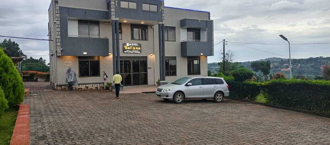A modern hotel with a paved entrance, a car parked in front, and a person walking towards the entrance.