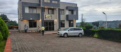 A modern hotel with a paved entrance, a car parked in front, and a person walking towards the entrance.