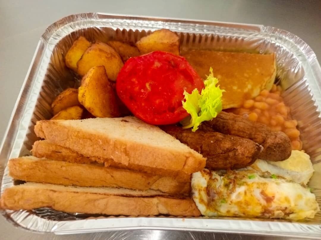 A meal tray with fried potatoes, a slice of tomato, beans, fried chicken, and a piece of fried fish.