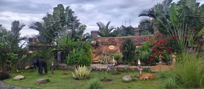 A lush garden with a stone wall, tropical plants, and a statue. - Hotel Bafana International  (Kalamba)