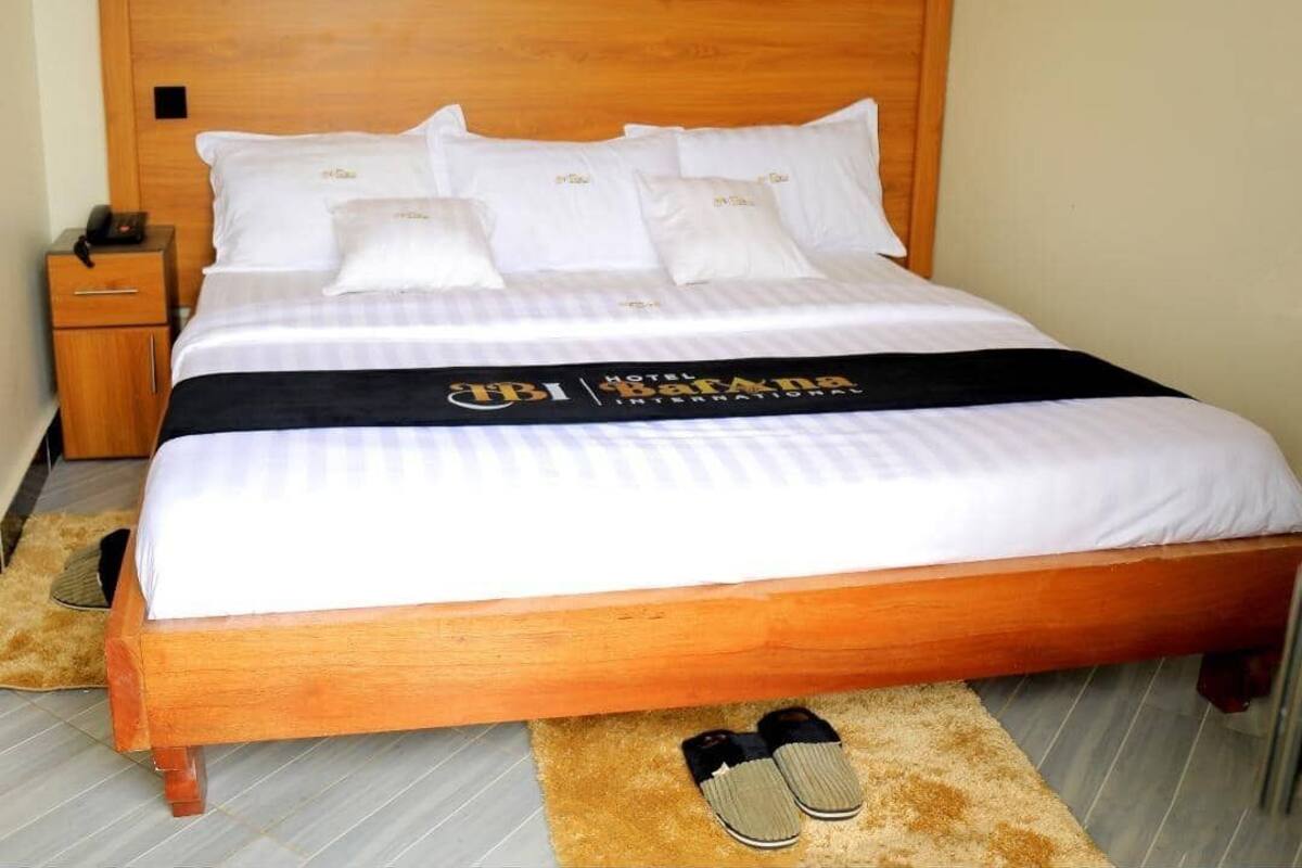 Una cama bien tendida con cabecera de madera, ropa de cama blanca y una colcha negra con un logotipo.