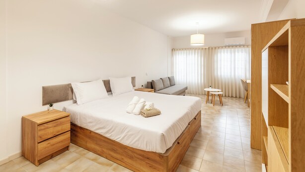 Ein modernes Hotelzimmer mit einem großen Bett, einem hölzernen Nachttisch, einem kleinen Tisch und einer Sitzecke mit Sofa und Sesseln.