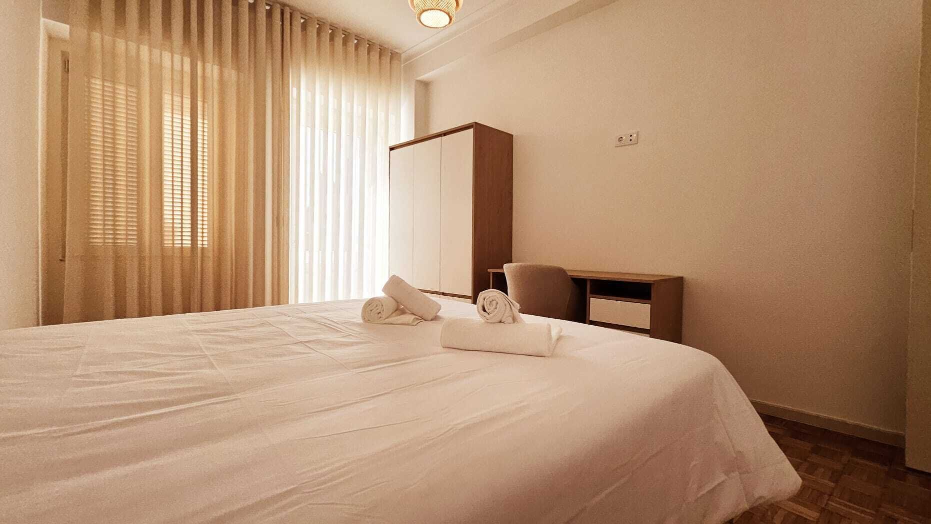 A hotel room with a large bed, a desk, and a chair.