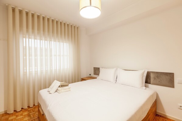 A neatly made bed with white linens, a wooden headboard, and a bedside table with a lamp. - Rooms4you 1 in historic center of Braga (Braga)