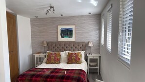 Une chambre à coucher comprenant un lit, deux tables de chevet, un ventilateur de plafond, une fenêtre avec des stores et un tableau accroché au mur.