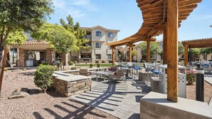 An outdoor patio area with stone seating, a pergola, and a building in the background. - ASU & Mill Ave | Sunny Getaway | Hot Tub & Gym (Tempe)
