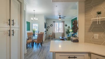 A modern kitchen with white cabinets, a dining area with wicker chairs, and a ceiling fan.