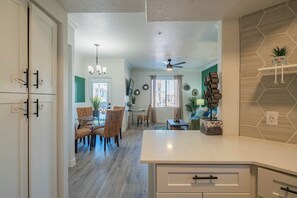 A modern kitchen with white cabinets, a dining area with wicker chairs, and a ceiling fan.