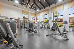 A gym with various exercise machines, large windows, and a ceiling with a geometric light fixture.