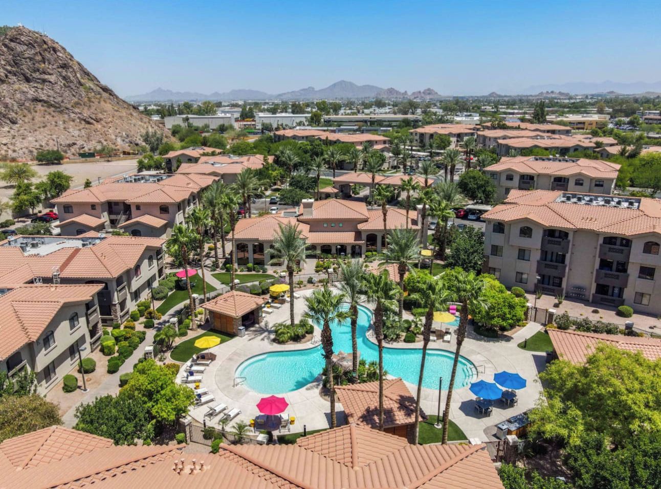 Un complejo turístico con varias edificaciones, una piscina central y palmeras.