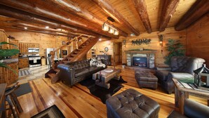 A log cabin interior with a living room, fireplace, and kitchen area.