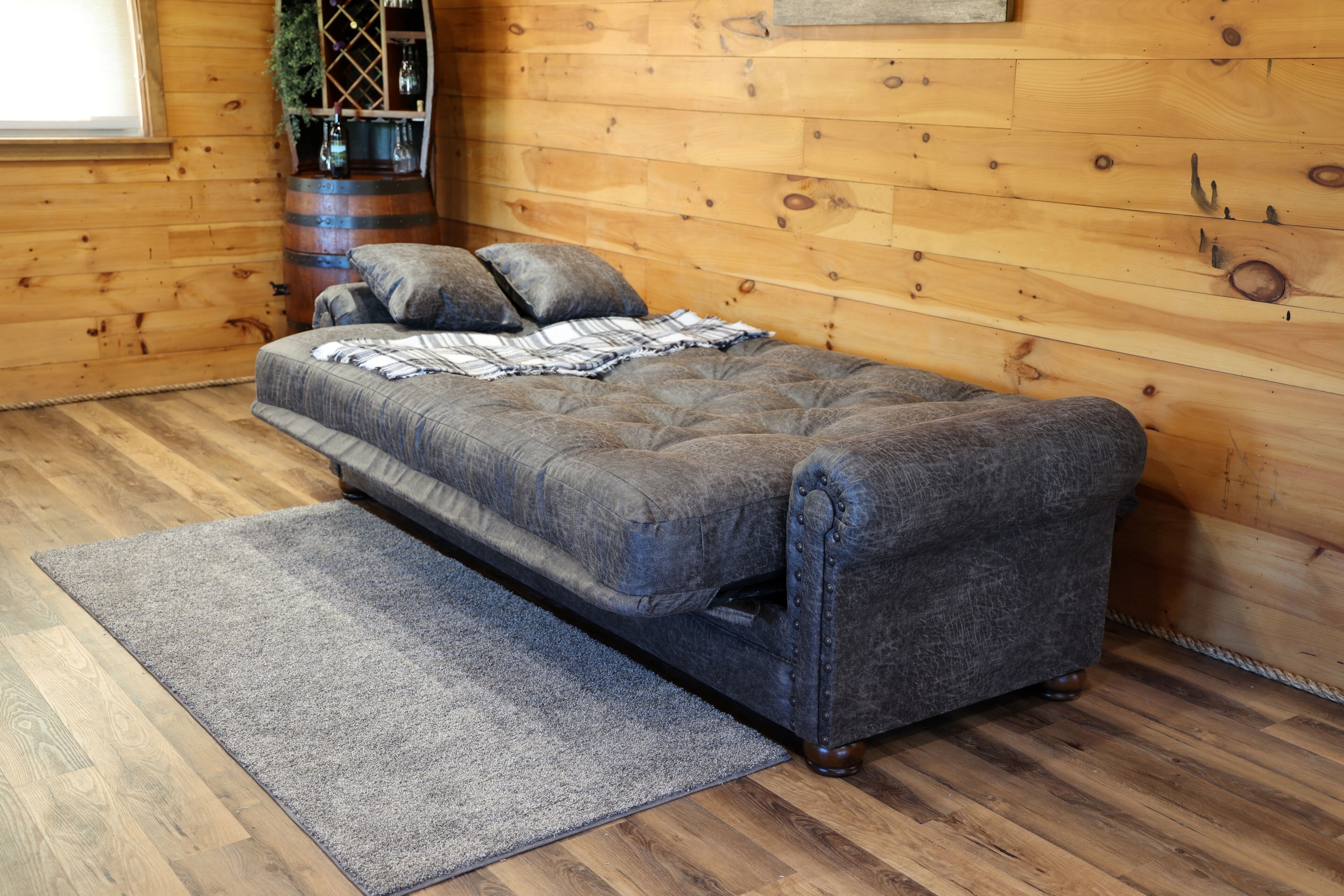 A cozy room with a grey sofa, a grey rug, wooden flooring, and a wooden wall.