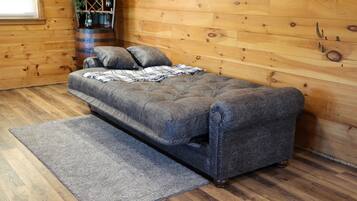 A cozy room with a grey sofa, a grey rug, wooden flooring, and a wooden wall.