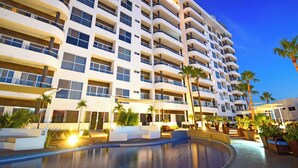 Un hotel de varios pisos con balcones, piscina y palmeras.