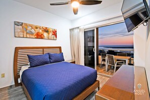 A hotel room with a bed, a ceiling fan, a painting, a TV, and a balcony with a view.