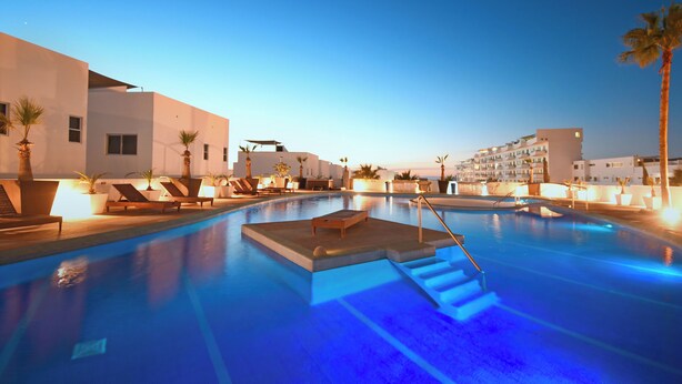 Un área de piscina con sillones, una tumbona y una pequeña terraza.