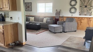 Una sala de estar moderna con un sofá gris, una mesa de centro y una alfombra. Se observa un mueble de madera con un jarrón de flores encima.