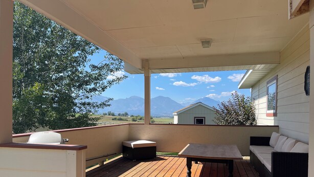 Una terraza techada con piso de madera, una mesa, un sofá y una parrilla.