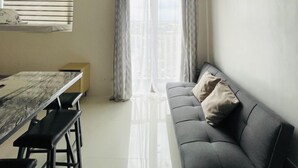 A modern living room with a sofa, a dining table with benches, and a large window with curtains. - WV Towers Studio with Balcony and Pool (Iloilo City)