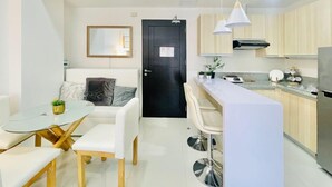 Cocina moderna con una isla central, taburetes blancos de bar, una mesa de comedor con sillas y una puerta negra con un espejo arriba.