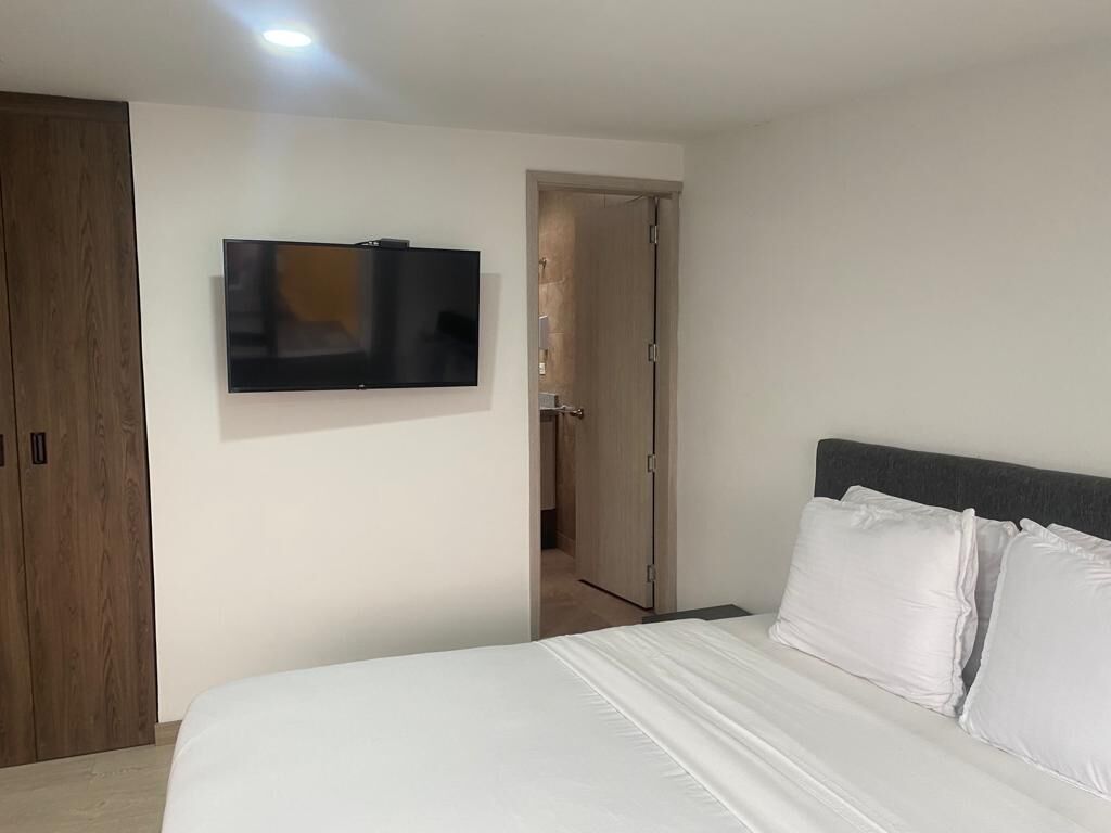 A bedroom with a bed, a television mounted on the wall, and a wardrobe.