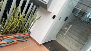 A modern building entrance with a glass door, a tiled floor, and a colorful planter with striped plants. - Spacio30 (Bogotá)