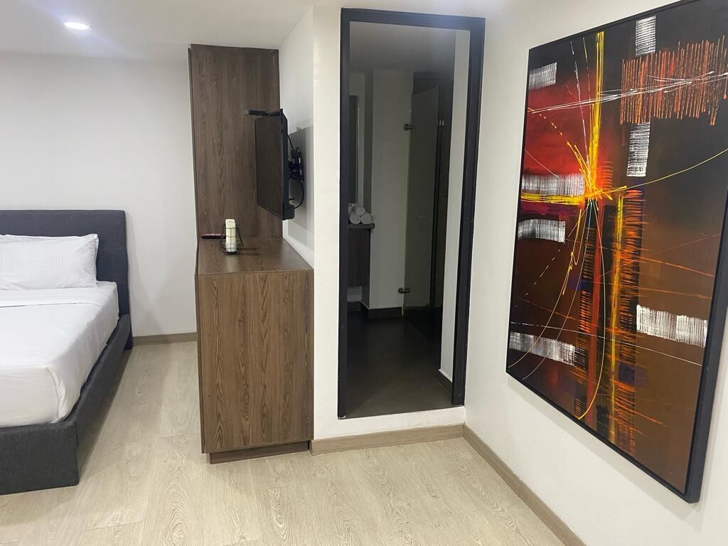 A modern bedroom with a bed, a wooden wardrobe, a mirror, and a large abstract painting on the wall.