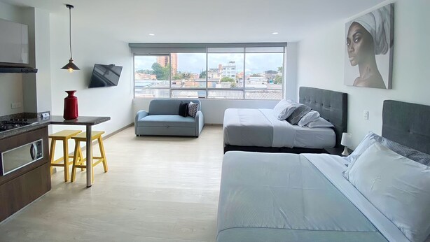 A modern apartment with a kitchen, a dining area, a sofa, a bed, and a large window offering a city view. - Spacio30 (Bogotá)