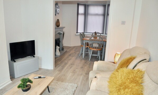 A living room with a TV, a sofa, a fireplace, and a dining area with chairs.