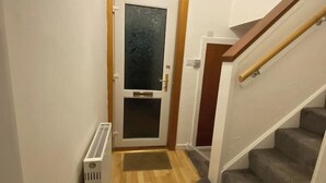Un couloir étroit doté d’un plancher en bois, d’un radiateur blanc et d’une porte avec un panneau en verre dépoli.