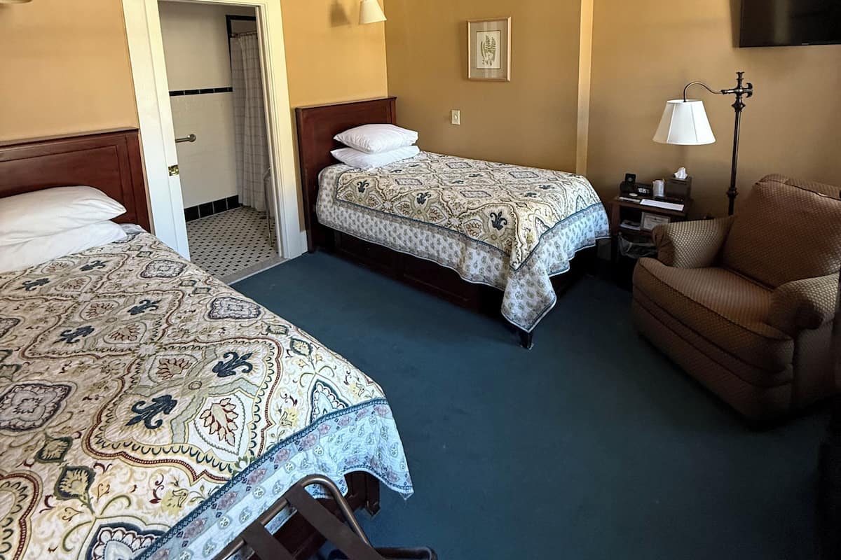 A hotel room with two beds, a sofa, a TV, and a lamp.