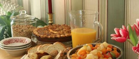 Une table de petit-déjeuner avec une tarte, une salade de fruits, des muffins et du jus.