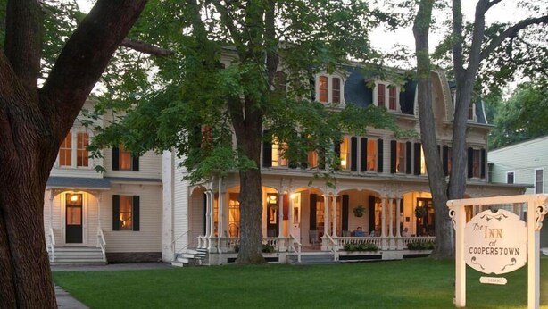 Un edificio de dos pisos con un porche y un letrero que dice "The Inn at Cooperstown".