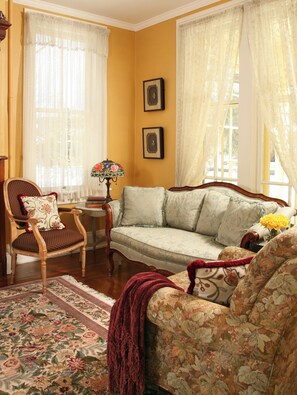 A living room with a sofa, armchairs, a small table with a lamp, and a rug.