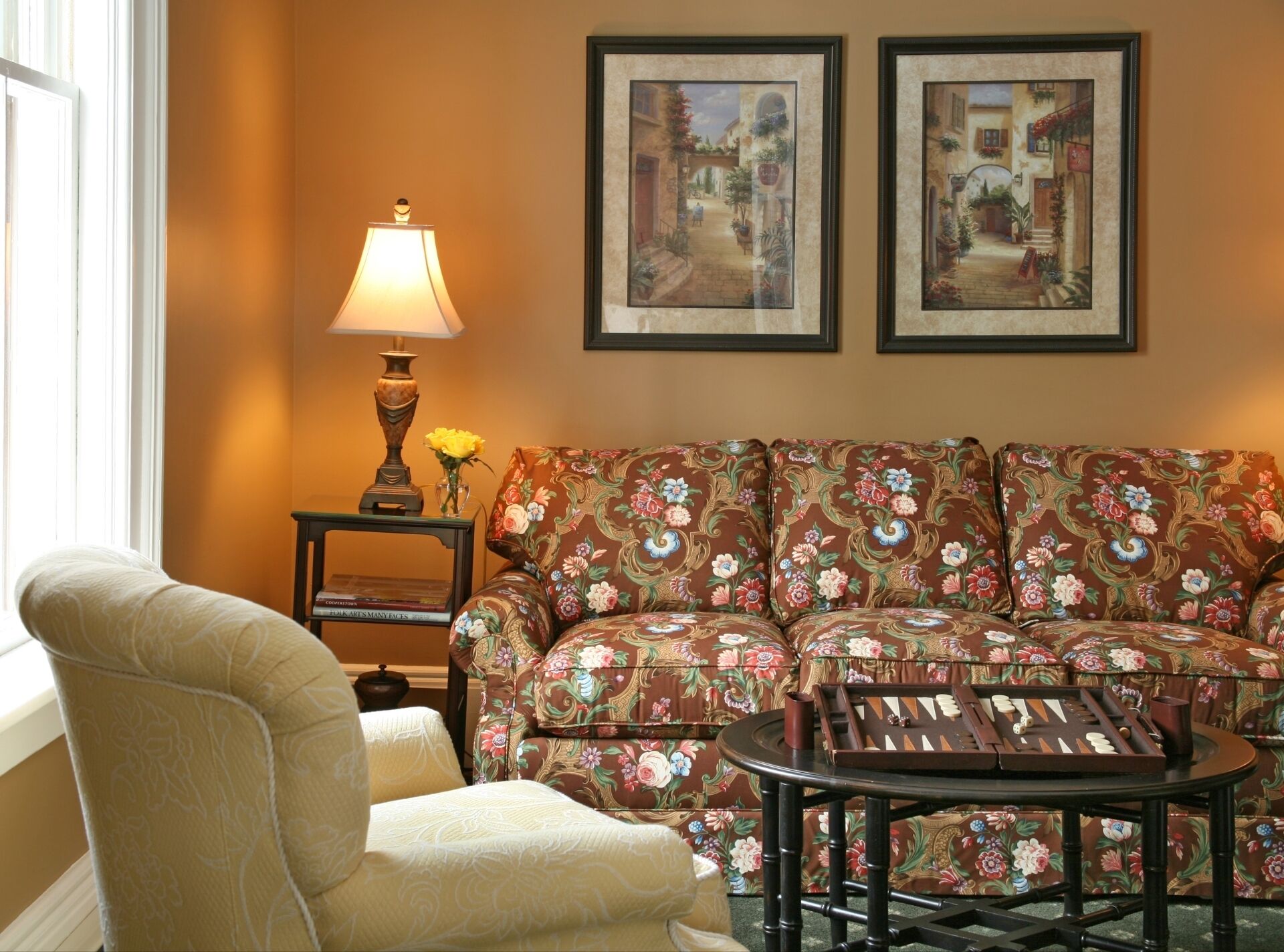 A living room with a floral sofa, a round coffee table, a lamp, and two framed pictures on the wall.