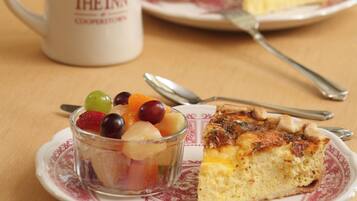 A breakfast setting with a slice of quiche, a fruit bowl, muffins, and a coffee mug labeled "The Inn".