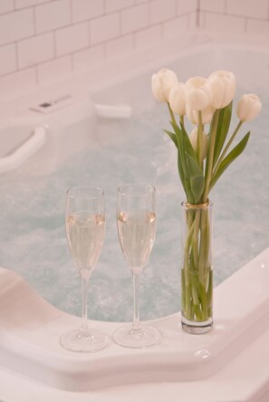 A bathtub with two champagne flutes and a vase of white tulips.
