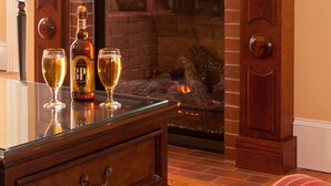 Una sala de estar con chimenea, televisor montado encima y una mesa con una botella y vasos.