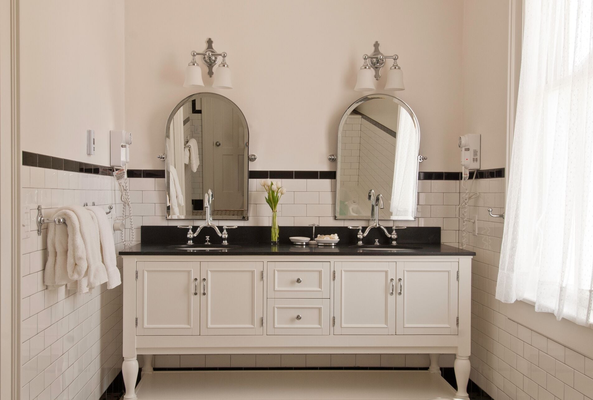 Une salle de bain avec un meuble-lavabo blanc, deux miroirs, un évier et un porte-serviettes.